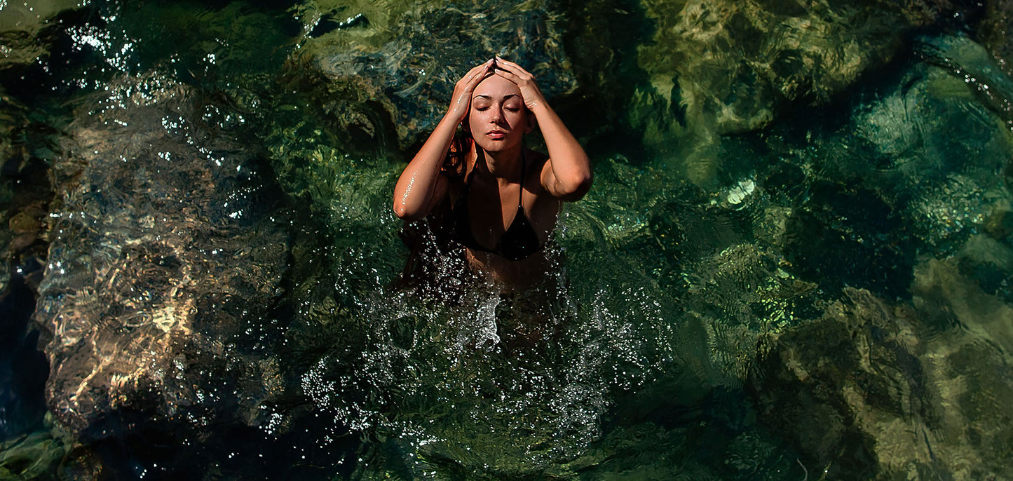 Beautiful woman emerging from tropical water, pulling her hair back from her face.